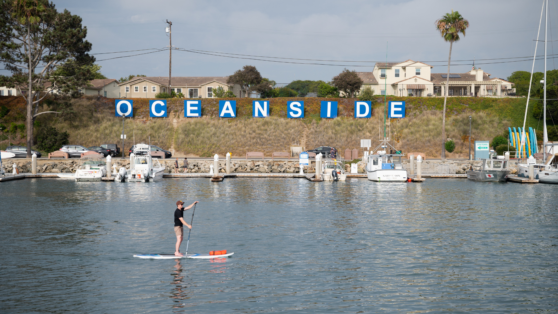 Image of a person paddle boarding in front of a Oceanside sign